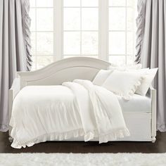 a white bed sitting in front of a window with curtains on either side of it