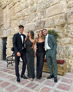 four people standing next to each other in front of a stone wall and planter