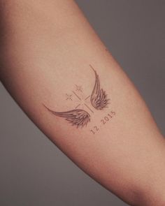 a woman's arm with a cross and wings tattoo on the left side of her arm