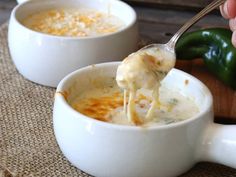 a spoon full of soup with cheese being lifted from it's bowl and another bowl in the background