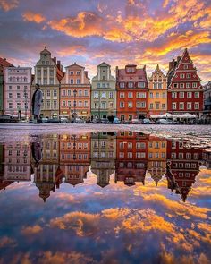 colorful buildings are reflected in the water on a cloudy day, with pink and orange clouds