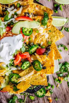 nachos topped with cheese, peppers and avocado on a wooden table