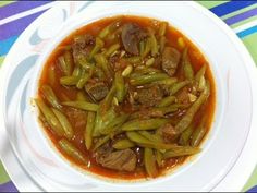 a white plate topped with green beans and meat in gravy next to a colorful table cloth