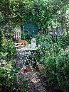 an outdoor table and chair in the middle of a garden with lots of greenery