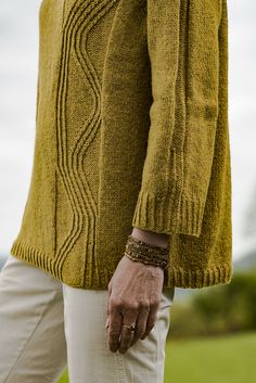 a man wearing a yellow sweater and white pants with his hand on his hip, standing in the grass