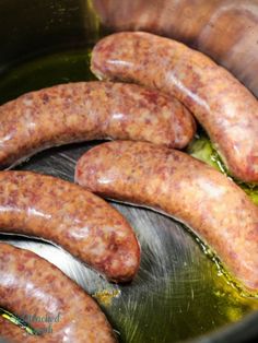 several sausages are cooking in a pot with green liquid on the bottom and sides