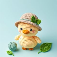 a small crocheted bird with a hat and green leaves on its feet next to a ball of yarn