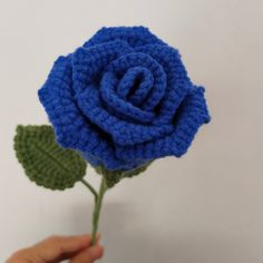 a crocheted blue rose being held by a person's hand on a white background