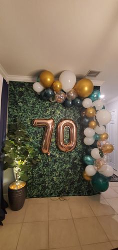 balloons and greenery decorate the entrance to an 70th birthday party with gold, green, and white balloons