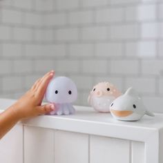 a person holding their hand out to three small toys on top of a white shelf