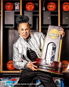 the woman is holding up her trophy in front of basketballs and lockers behind her