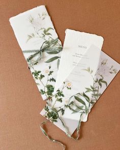 two folded cards with flowers and leaves on them, tied to each other next to a string