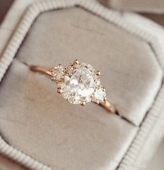 an engagement ring with three stones in it on a cushioned surface, sitting on top of a velvet box