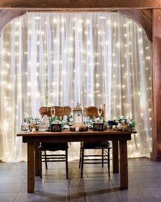 a wooden table topped with lots of chairs under a white curtain covered room filled with lights