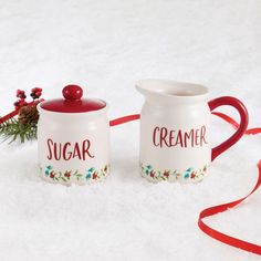 two creamers sitting on top of snow covered ground next to a christmas tree branch