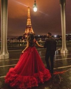 a man and woman standing in front of the eiffel tower at night wearing red dresses