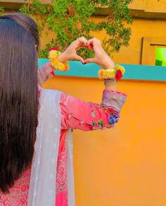 a woman standing in front of a yellow wall making a heart shape with her hands