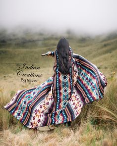 a woman with long black hair wearing a colorful dress and standing in the middle of a field