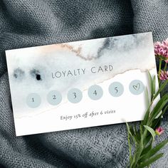 a business card sitting on top of a gray blanket next to some purple and white flowers