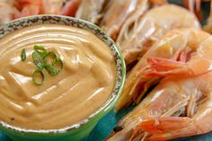 a green bowl filled with sauce next to shrimp and other foods on a blue surface