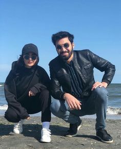 two people sitting on the beach posing for a photo