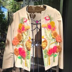 a white jacket with flowers on it is hanging from a rack in front of a window