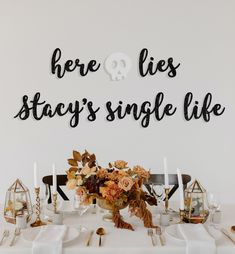 there is a white table with flowers and candles on it that says here lies stay's single life