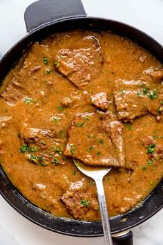 a skillet filled with meat and gravy on top of a white counter