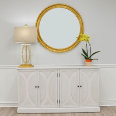 a white and gold sideboard with a round mirror on it next to a lamp