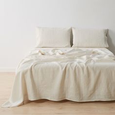 an unmade bed with two pillows on top of it in a white walled room