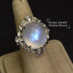 This large rare Moonstone Cabochon Ring is set in 14k solid gold and exhibits mesmerizing blue flash aduralescence. Scintillating diamonds surround this natural beauty!Ring Size: 5.75Total Weight: 13.65 gramsPrecious Metal: 14k solid goldPrecious stones:-Moonstone Center Stone: 18.5mm x 16.2mm, 23.05 carats-White Round Diamond: 0.4ct Collectible Oval Cabochon Moonstone Ring, Formal Moonstone Ring With Gemstone Accents, Elegant Collectible Moonstone Ring, Luxury Multi-stone Round Moonstone Ring, Celestial Multi-stone Oval Moonstone Ring, Formal Moonstone Cabochon Ring, Celestial Multi-stone Moonstone Oval Ring, Celestial Multi-stone Moonstone Ring, Formal Oval Multi-stone Moonstone Ring