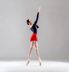 a woman in red skirt and black top doing a ballet move with her arms outstretched