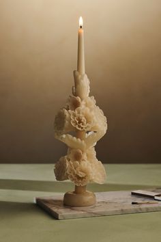 a candle that is sitting on top of a wooden block with flowers in it and a book nearby