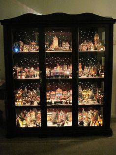 a lighted display case filled with lots of christmas decorations on top of glass shelves in a living room