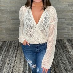 a woman standing in front of a brick wall wearing ripped jeans and a white sweater