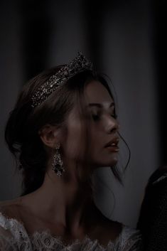 a woman wearing a tiara and looking down at her dress while standing in the dark