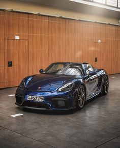 a blue sports car parked in front of a wooden wall with two doors on the other side