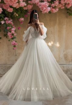 a woman in a wedding dress taking a selfie with her cell phone while standing next to pink flowers