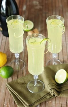 three glasses filled with lemonade sitting on top of a table next to limes