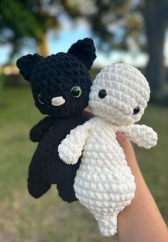 two crocheted stuffed animals are held in someone's hand, one is black and the other is white