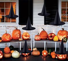 a group of pumpkins sitting on top of a white bench next to black witches hats