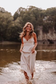 a woman in a white dress is walking through the water