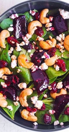 a salad with beets, walnuts and spinach in a black bowl on a white table