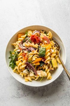 a white bowl filled with pasta and vegetables on top of a table next to a fork