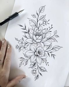 a woman's hand is holding a pen and drawing flowers on paper with black ink