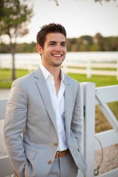 a man standing in front of a white fence wearing a gray suit and brown tie