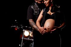 a pregnant woman standing next to a man on a motorcycle with his arm around her belly