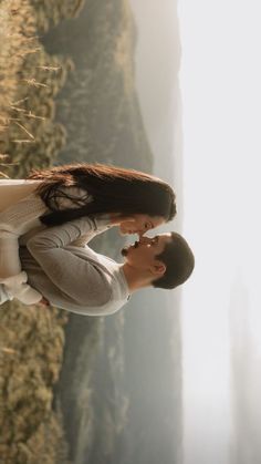 a man and woman standing next to each other in front of a cliff with grass