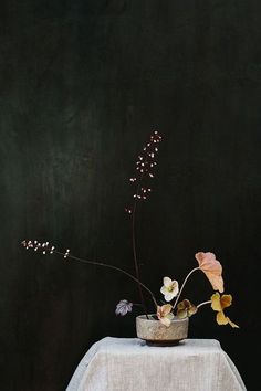 a vase with flowers sitting on top of a white table cloth covered table next to a black wall