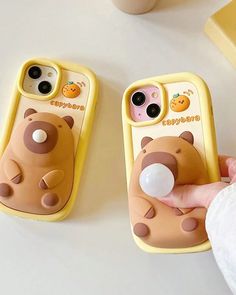 someone is holding two cell phones in their hands, one has a bear design on it